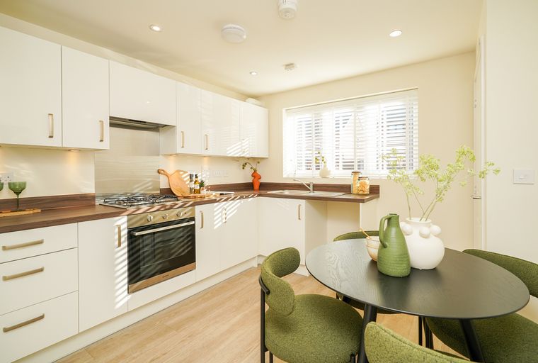 A modern kitchen with white cabinets, a gas stove, and a dining table with green chairs.