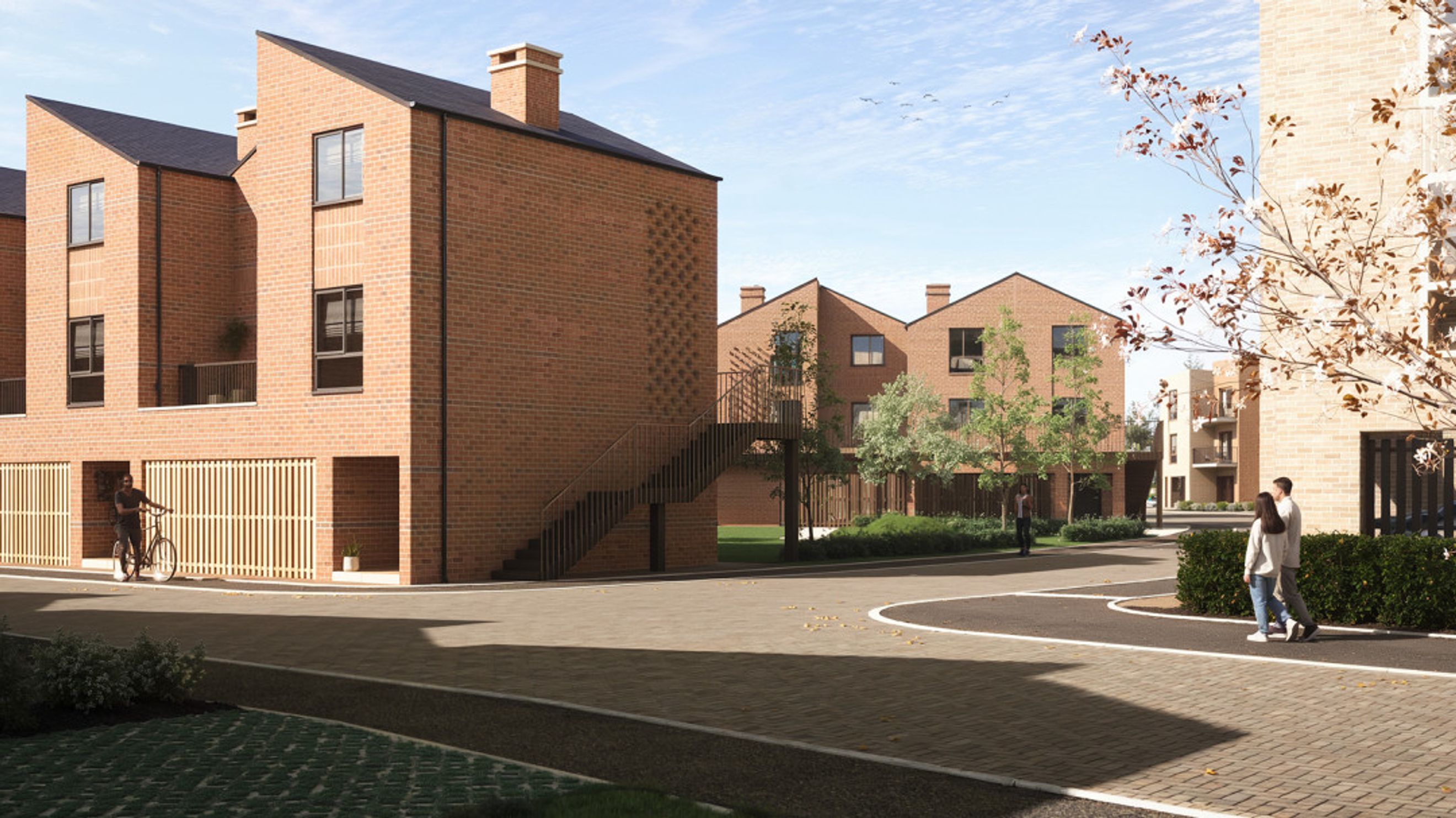 A street view of a modern housing development with brick townhouses, paved pathways, and trees.
