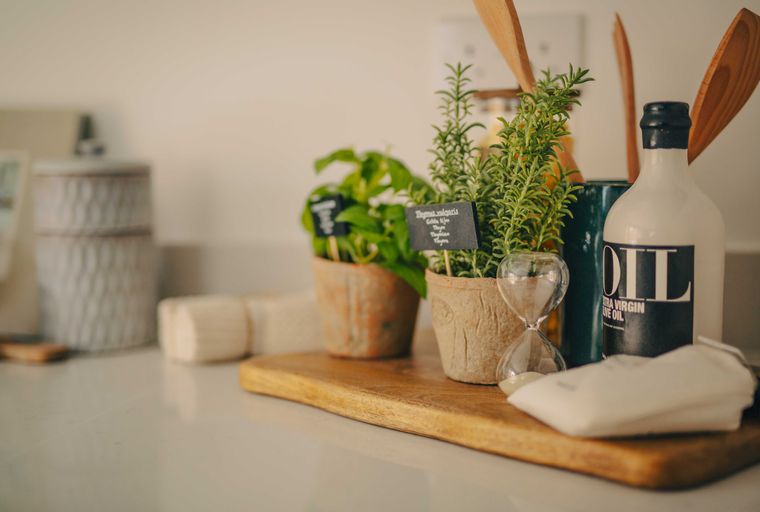 A kitchen counter with potted herbs, olive oil, and wooden utensils.