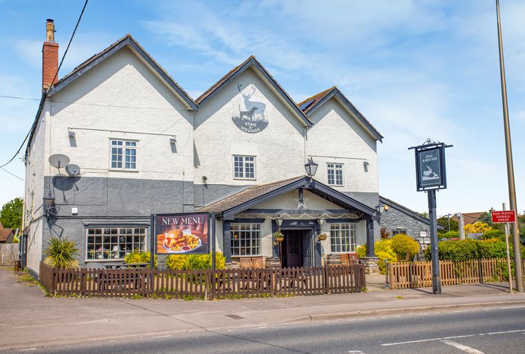 A pub called The Stag & Hounds with a new menu sign and outdoor seating.