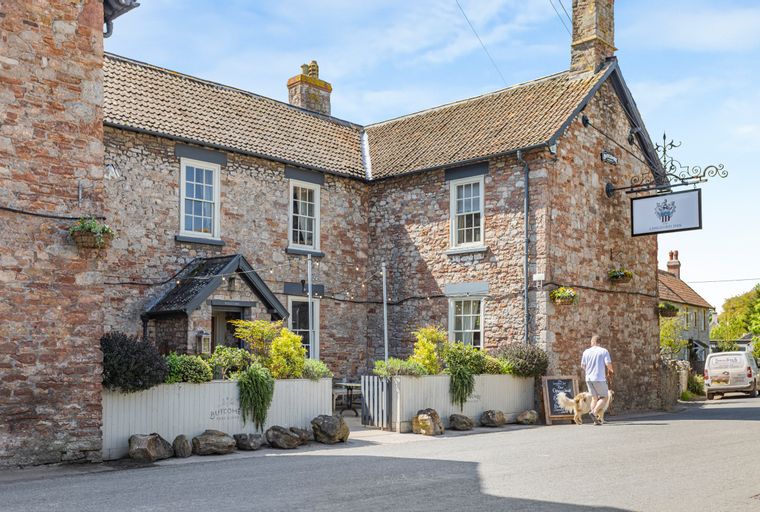 A man walks his dog past a stone building with a sign that says 'LANGFORD INN'.