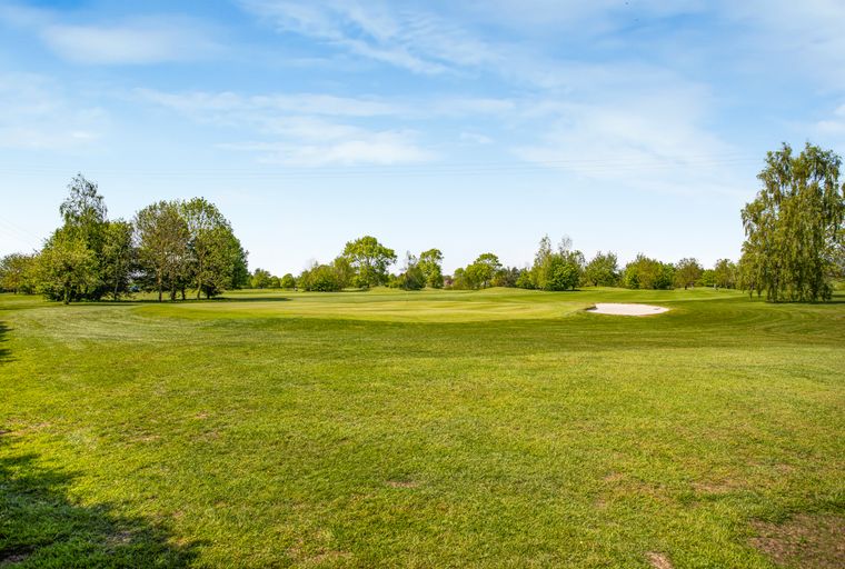A golf course with green fairways, trees, and a sand trap under a blue sky.