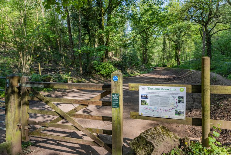 A wooden gate and signpost mark the entrance to a wooded walking trail called The Limestone Link.