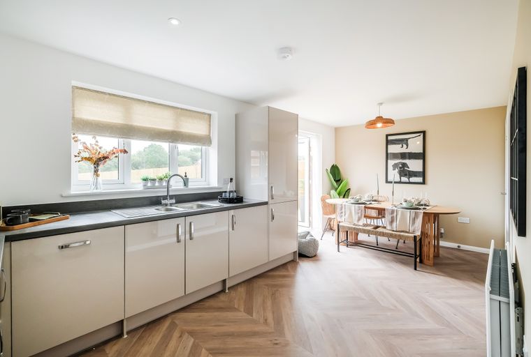 A kitchen and dining area with cream cabinets, a double sink, a dining table, and herringbone flooring.