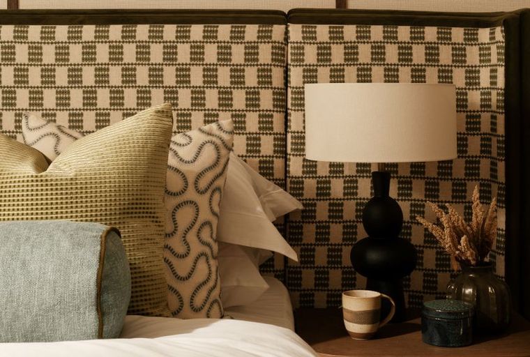 A bedroom with a headboard, pillows, and a bedside lamp.