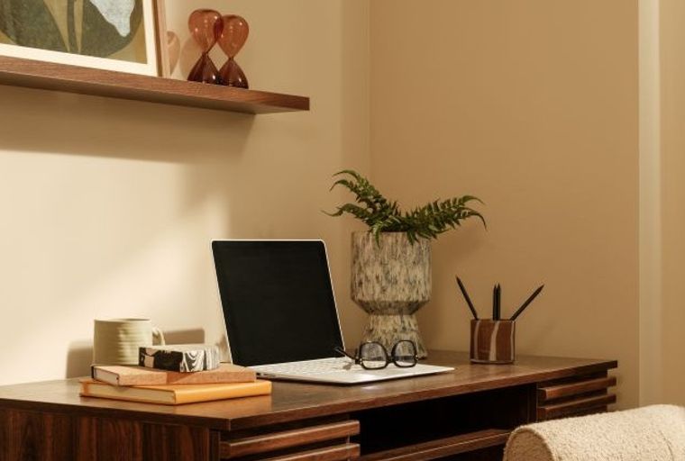 A desk with a laptop, books, a mug, glasses, and a plant.