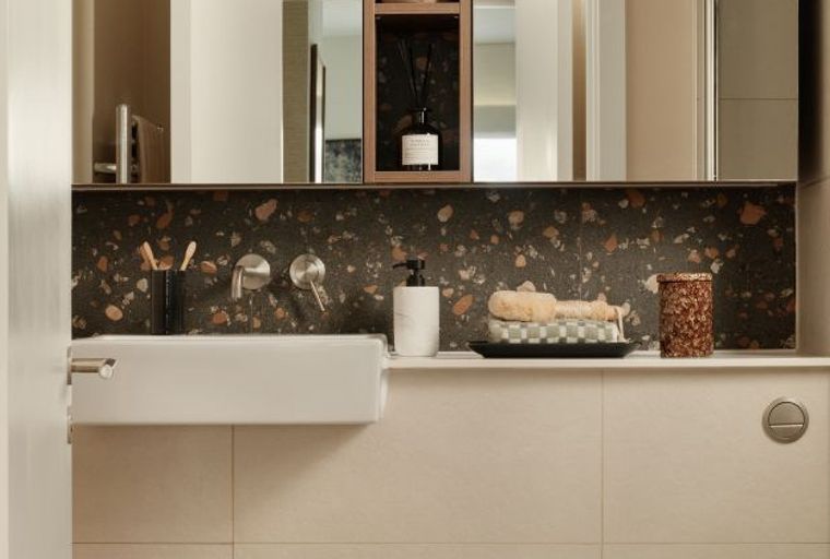 A bathroom with a sink, faucet, soap dispenser, and decorative items on a shelf.