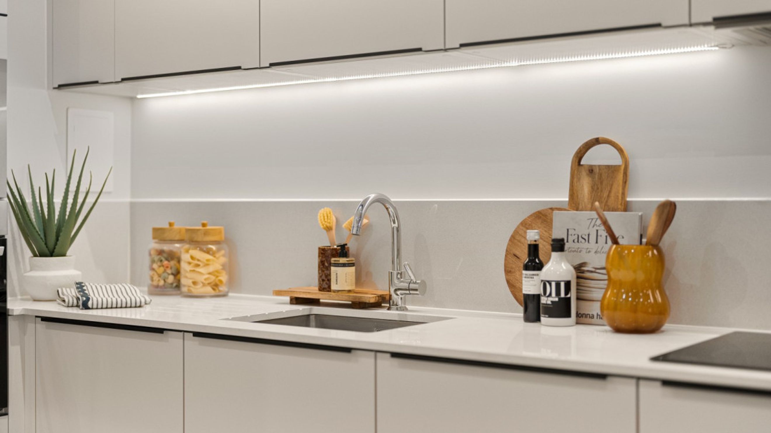 A modern kitchen counter with a sink, faucet, jars of pasta, and decorative items.