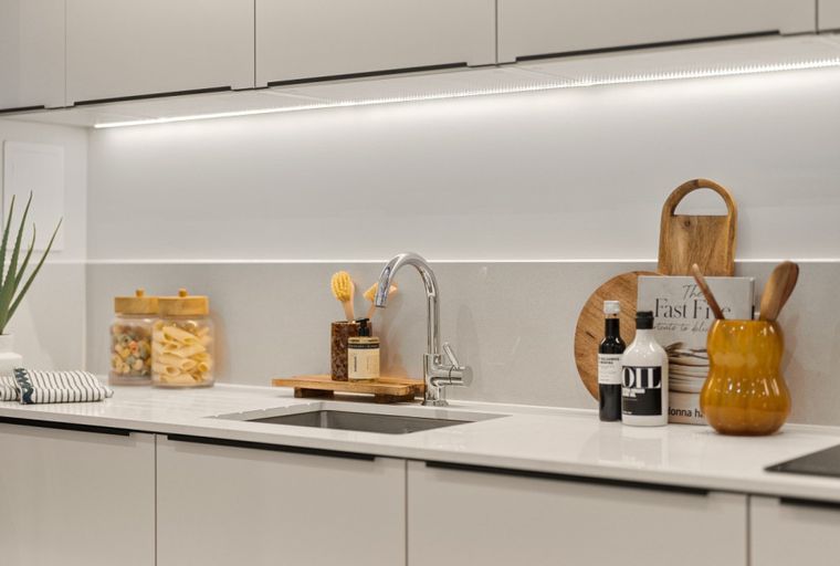 A modern kitchen counter with a sink, faucet, jars of pasta, and decorative items.