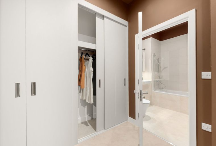 A hallway with a closet and an open bathroom door revealing a toilet and bathtub.