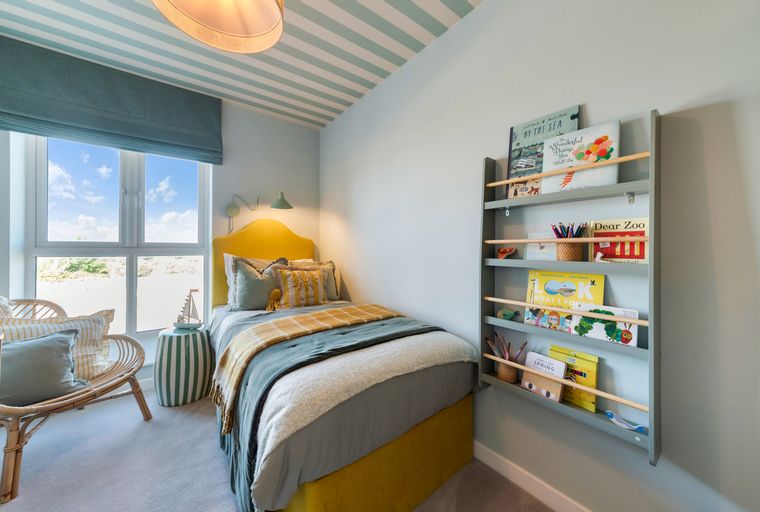 A child's bedroom with a bed, a chair, a window, and a bookshelf.