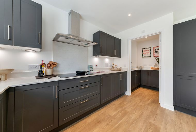 A modern kitchen with dark grey cabinets, a stainless steel range hood, and a white countertop.
