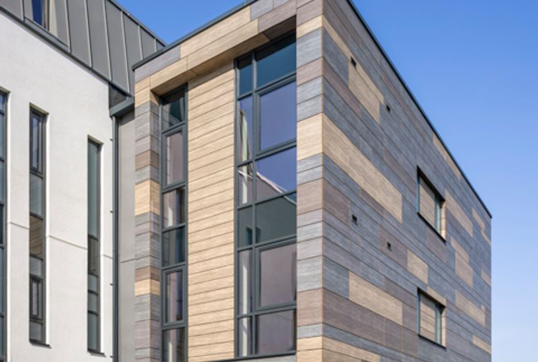 A modern building with a multi-toned facade and large windows, featuring a covered parking area on the ground floor.