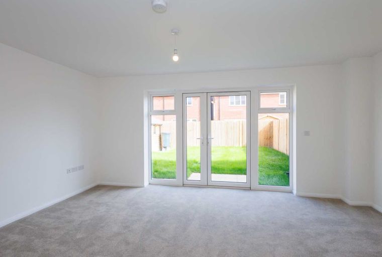 A living room with grey carpet, white walls, and double doors leading to a garden.