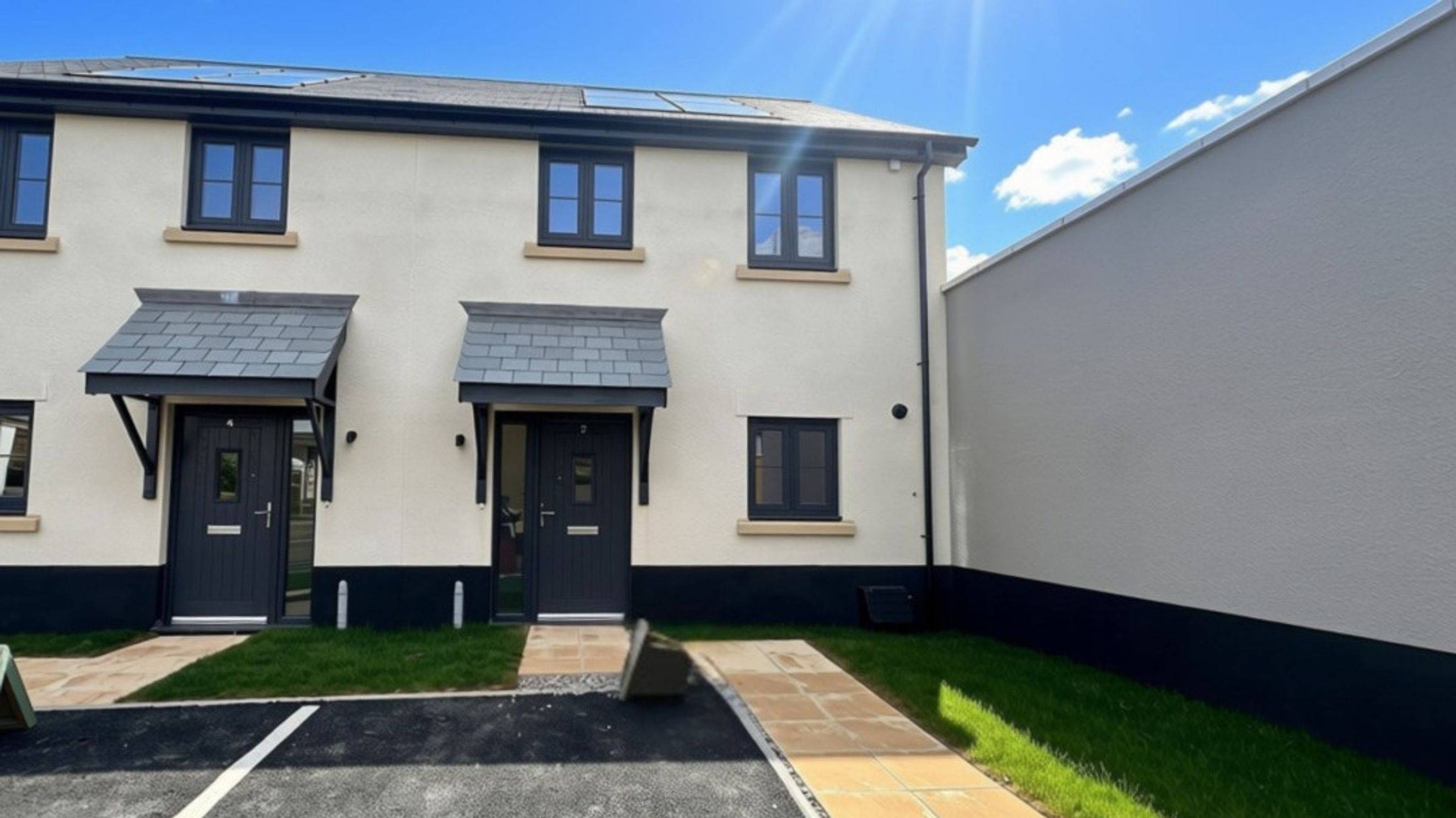 A row of modern townhouses with cream-colored exteriors, dark grey doors, and windows, under a bright blue sky.