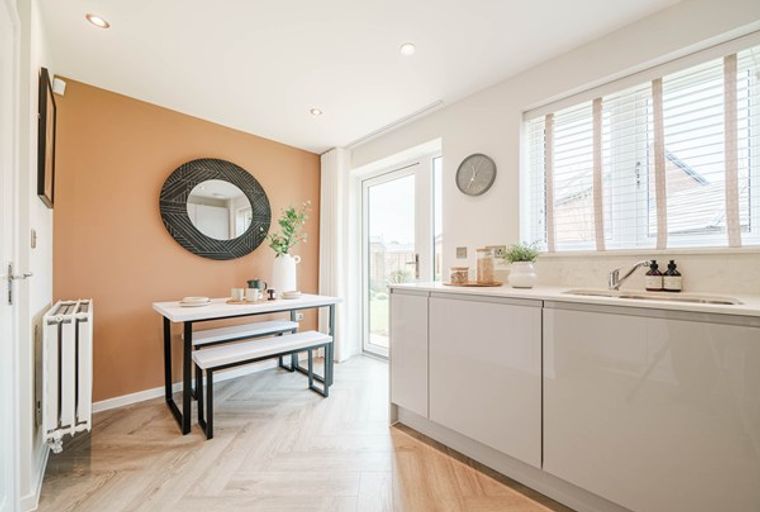 A dining area and kitchen with a table, benches, a mirror, and kitchen cabinets.