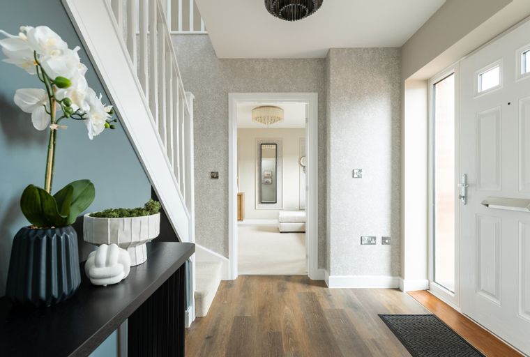 A hallway with a staircase, a front door, and an open doorway leading to another room.