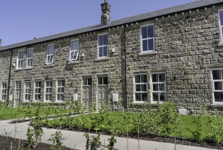 A row of stone-built houses with white-framed windows and a garden in front.