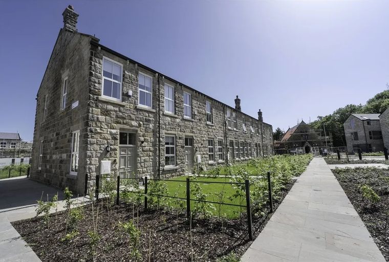 A row of stone-built houses with gardens and a paved walkway.