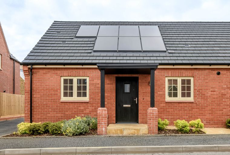 A brick house with a black front door, two windows, and solar panels on the roof.