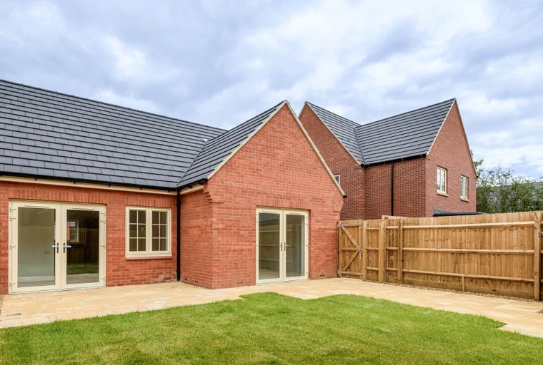 A newly built brick house with a backyard, patio, and wooden fence.