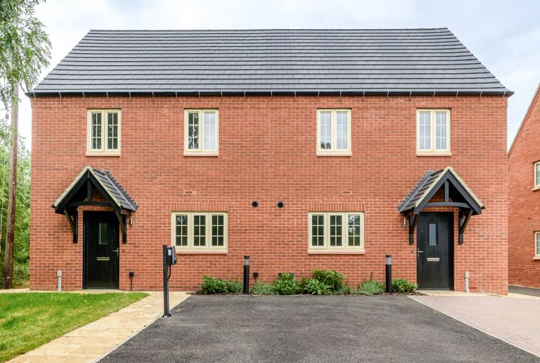 A pair of red brick semi-detached houses with black front doors and light cream windows.