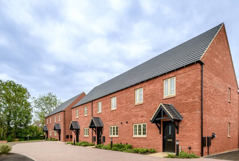 A row of new brick houses with grey roofs under a cloudy sky.