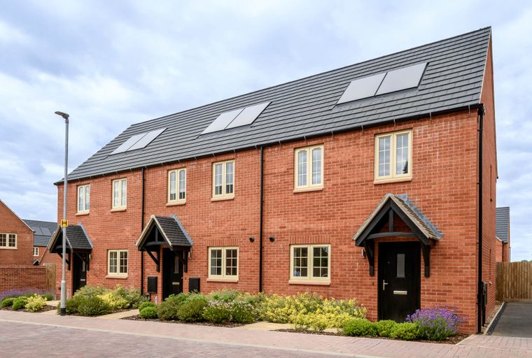 A row of modern red brick houses with grey tiled roofs and cream-framed windows.