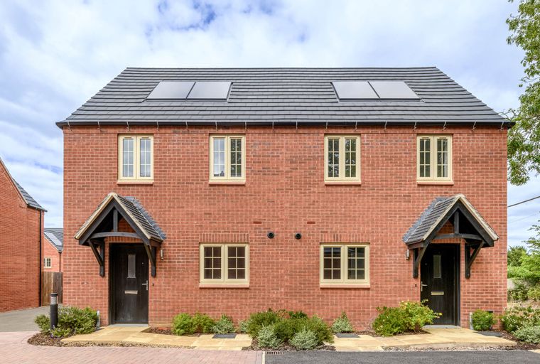 A pair of new red brick semi-detached houses with black front doors and cream windows.