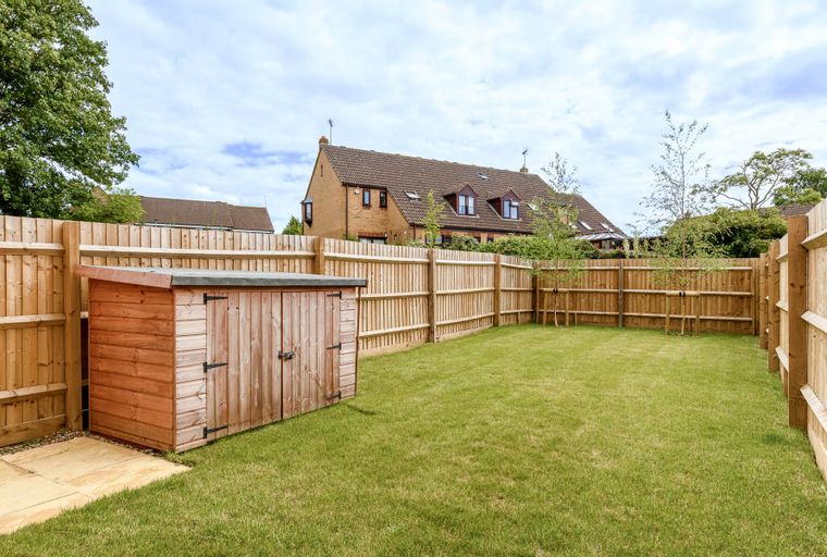 A backyard with a wooden shed, a lawn, and a wooden fence.