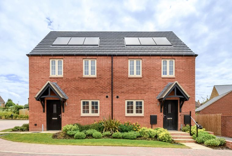 A pair of red brick semi-detached houses with dark doors, cream windows, and solar panels on the roof.