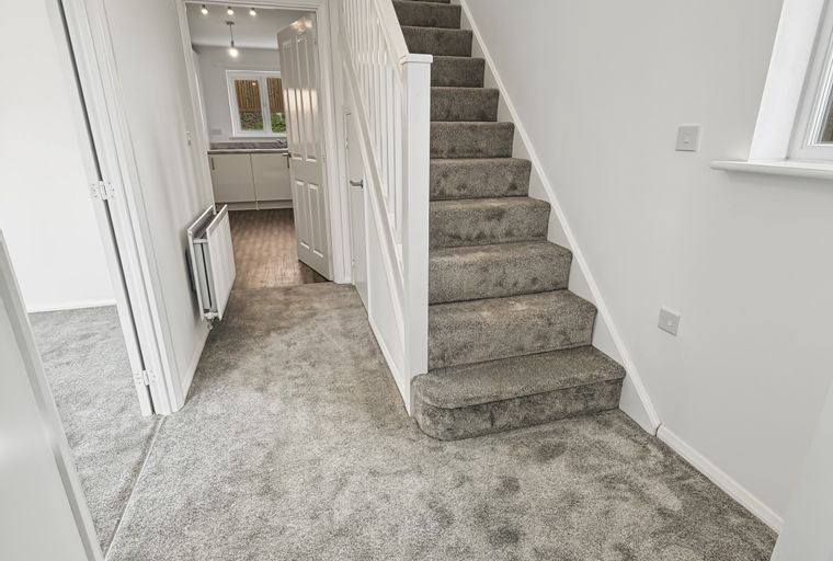 A hallway with a carpeted staircase and a doorway leading to a kitchen.