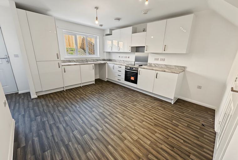 A modern kitchen with white cabinets, a marble-effect countertop, and wood-effect flooring.