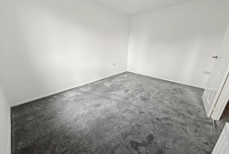 A room with white walls and grey carpet.