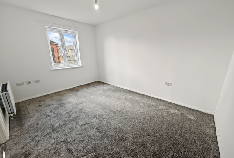 A bedroom with a window, carpet, and electrical outlets.