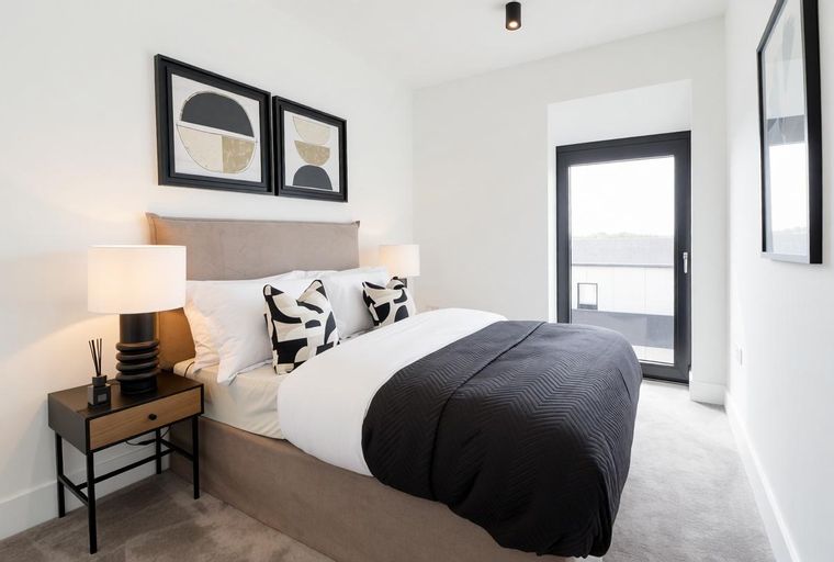 A bedroom with a bed, pillows, lamps, and artwork.