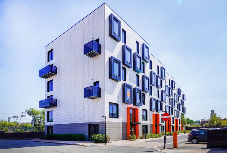 A modern apartment building with white tiled exterior, protruding windows, and balconies.