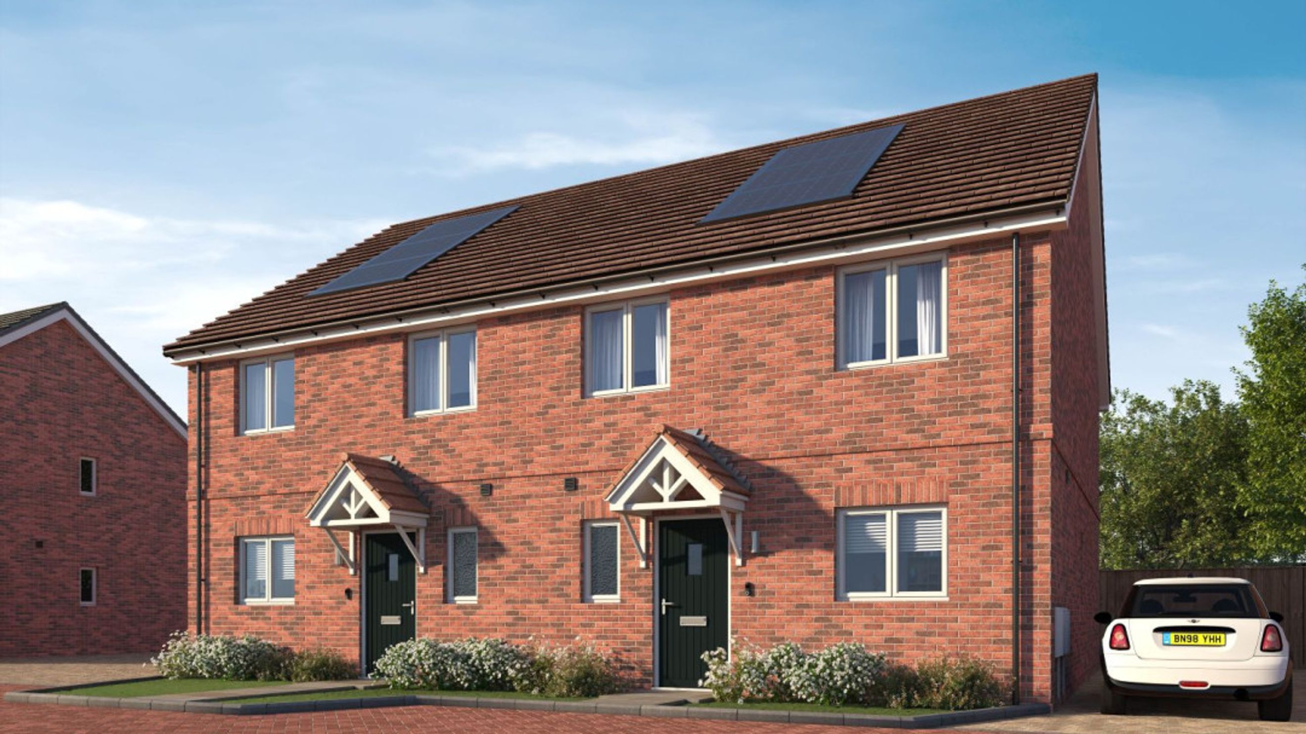 A pair of red brick semi-detached houses with solar panels on the roof and a white car parked in the driveway.