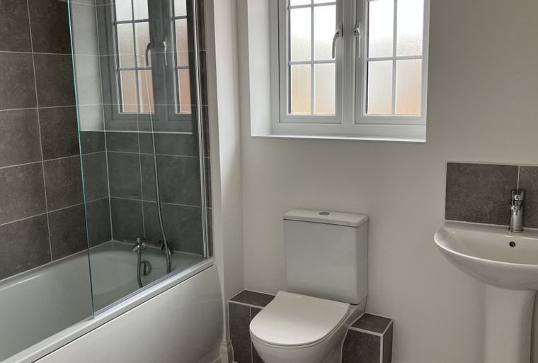 A bathroom with a bathtub, shower screen, toilet, sink, and a window.