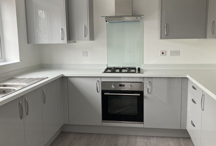A modern kitchen with grey cabinets, a white countertop, a sink, and an oven.