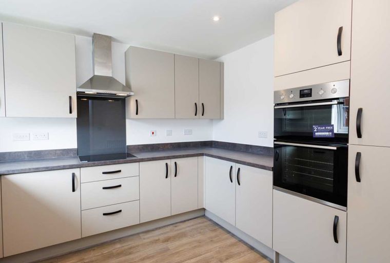 A modern kitchen with cream cabinets, a stainless steel range hood, and a double oven.