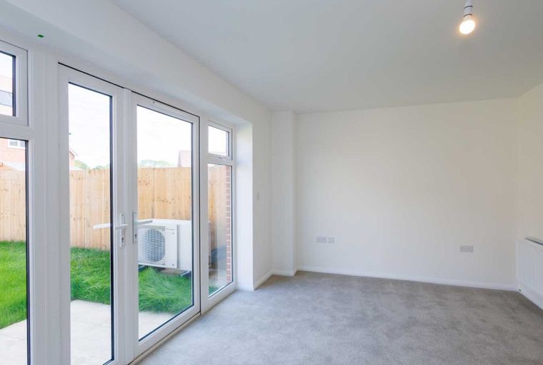 A living room with large glass doors opening to a garden, grey carpet, and a white radiator.