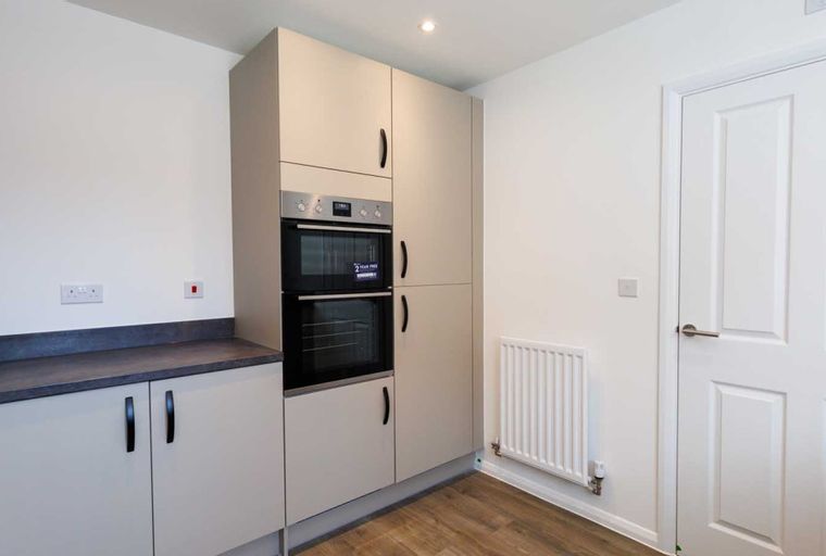 A kitchen with built-in ovens, cabinets, a countertop, and a radiator.