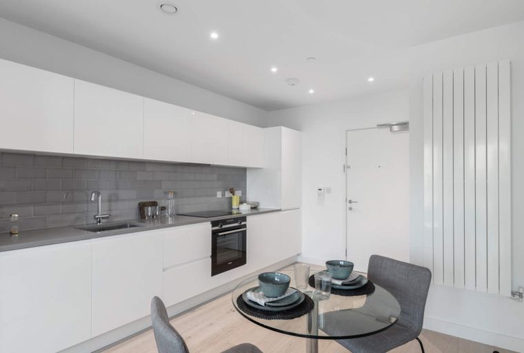 A modern kitchen with white cabinets, a grey tiled backsplash, and a dining table set for two.