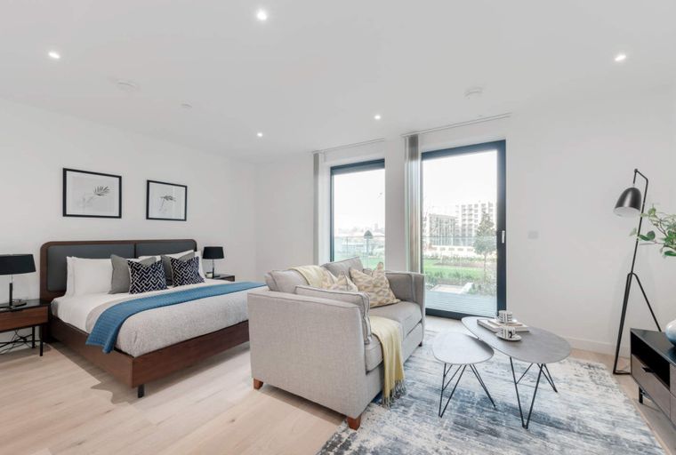 A studio apartment with a bed, sofa, coffee table, and large windows.