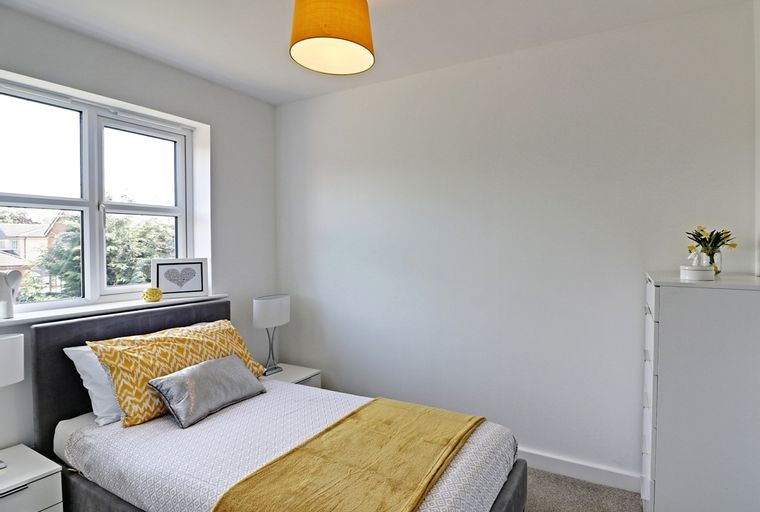 A bedroom with a bed, pillows, a window, and a dresser.