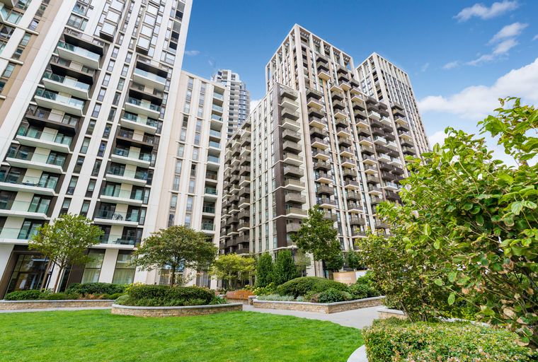 A view of modern apartment buildings with balconies and a landscaped garden in the foreground.