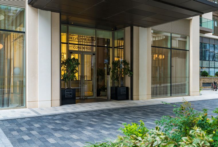 A modern building entrance with glass doors, potted trees, and signage for Belvedere Row and Concierge.