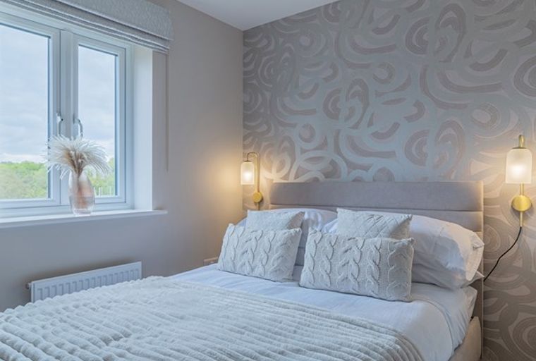 A bedroom with a bed, pillows, lamps, and a window.