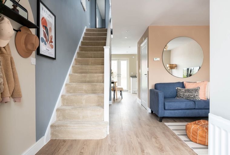 A hallway with a staircase, a blue sofa, and a round mirror.